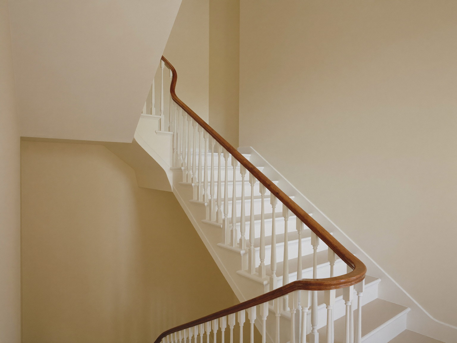 A finished repainted stair hall in an established Natick colonial: soft warm cream walls over smooth restored plaster, bright white balusters with a