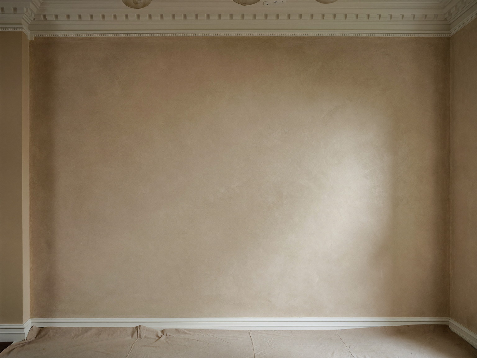 New skim-coat plaster drying under soft raking light in an established colonial room, smooth flat even finish, tidy canvas drop cloth below, crisp white