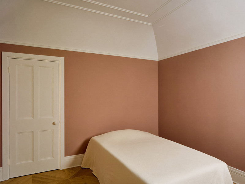 A repainted bedroom in an established Natick colonial: soft clay-rose walls, bright white trim and paneled door, smooth restored plaster in raking light,