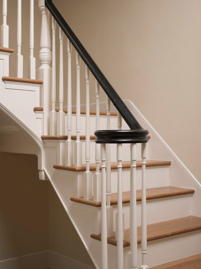 A refinished basement stair in an established colonial: crisp white risers and stringers, warm oak treads, a simple round black painted handrail on plain