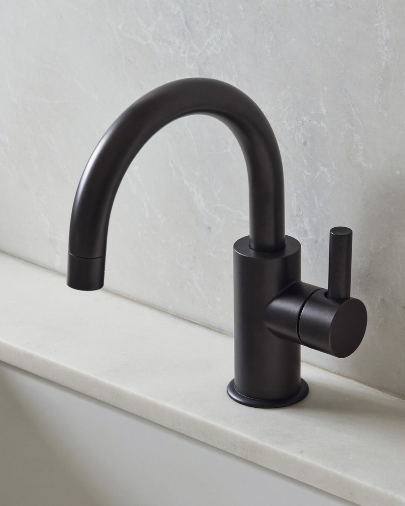A matte black bathroom faucet with a smooth arched spout and lever handle mounted on honed white stone, macro photograph from a slight angle, smooth