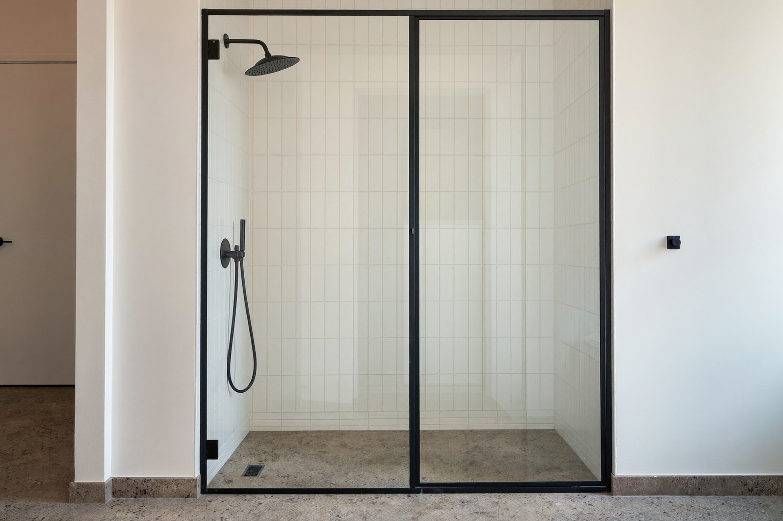 Wide photograph of a walk-in shower behind a matte black framed glass panel in a renovated suburban bathroom: warm white vertical stacked tile, matte