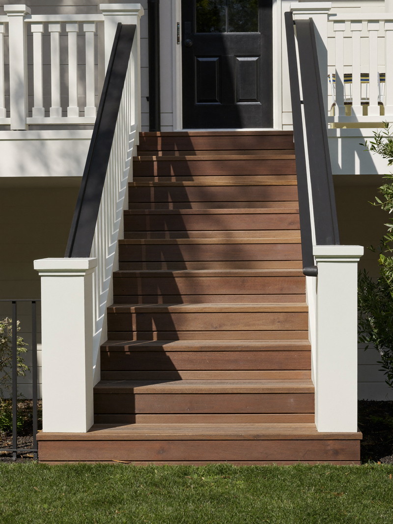 Newly built deck stairs on an established suburban colonial: warm brown composite treads, crisp white risers and square balusters, simple black handrail,