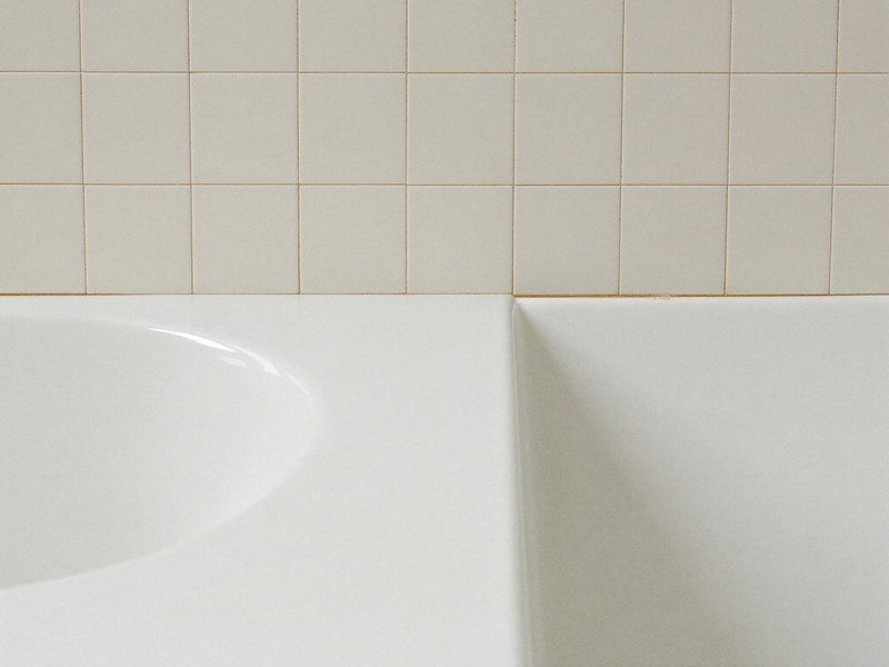 A clean bright white bathtub edge meeting warm white ceramic wall tile, the joint freshly finished, smooth and tidy, completely bare tub edge, soft