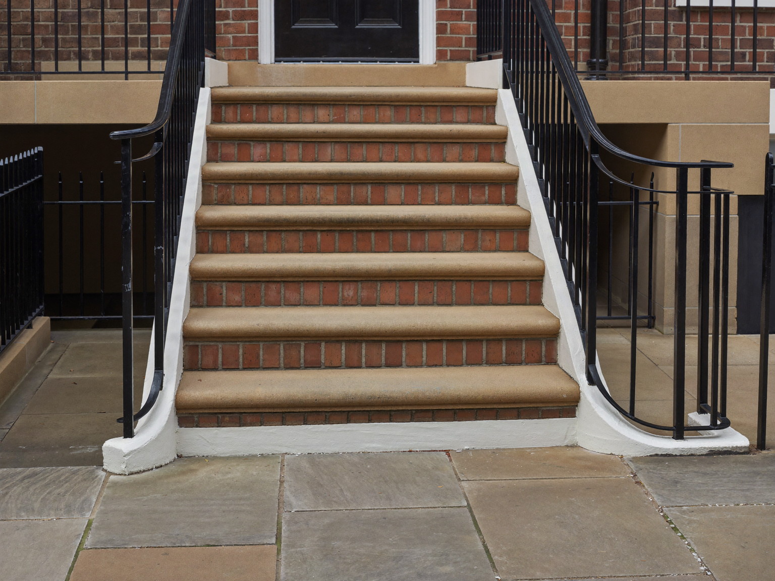 Repaired front entry steps of an established Needham colonial: brick treads, crisp white risers, a simple repainted black iron handrail, stone walk below,
