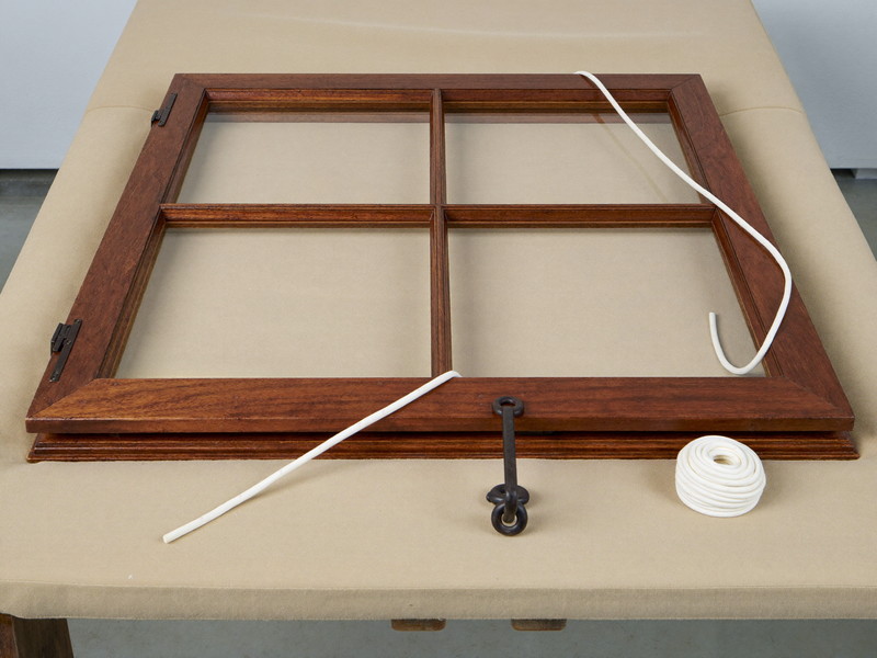 A colonial double-hung wooden sash window mid-repair: sash tilted open on a padded bench, smooth new cotton sash cord coiled neatly beside plain iron sash
