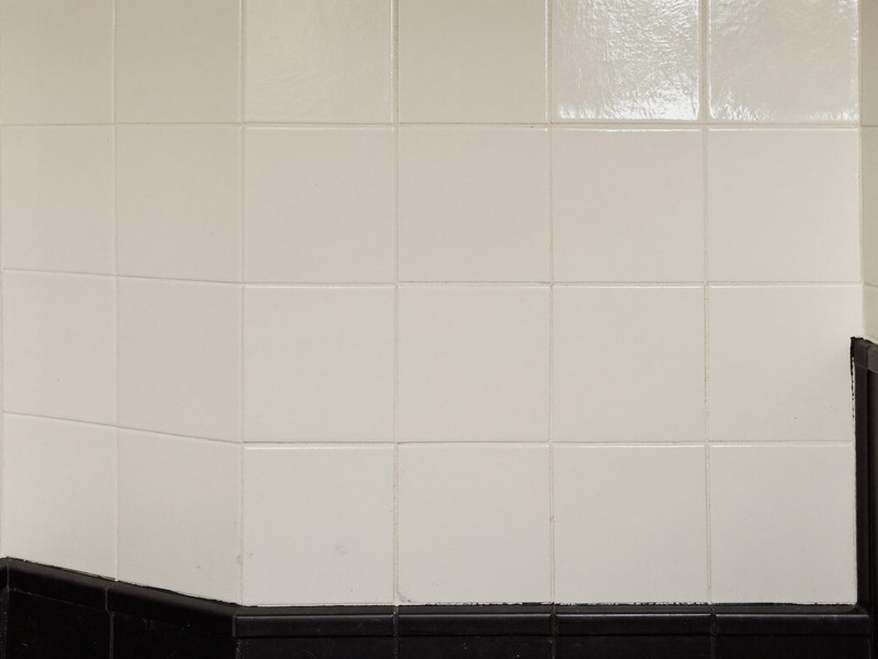 Freshly regrouted warm white ceramic tile in a suburban bathroom corner: clean bright grout lines, every tile flat and straight, matte black fitting at
