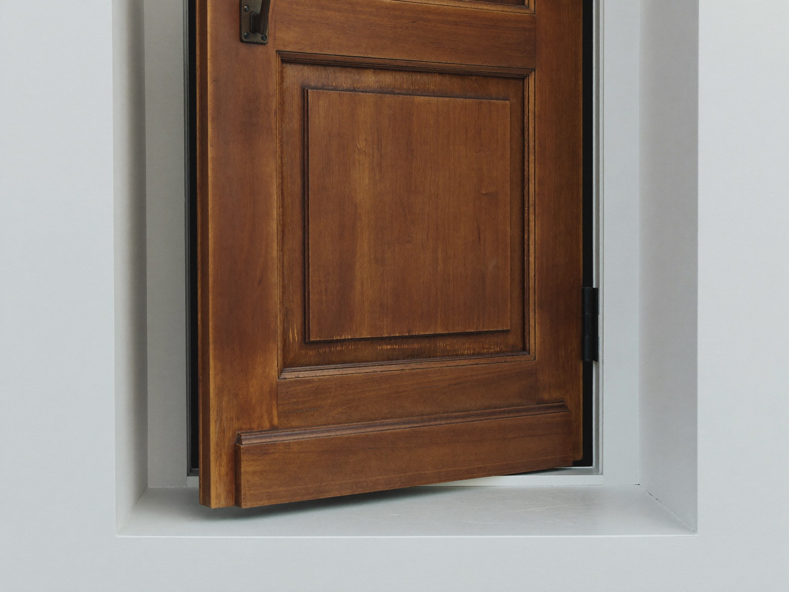 A traditional wooden front door resting ajar in its freshly serviced frame, seen from the side: smooth refreshed painted edge and one clean black hinge