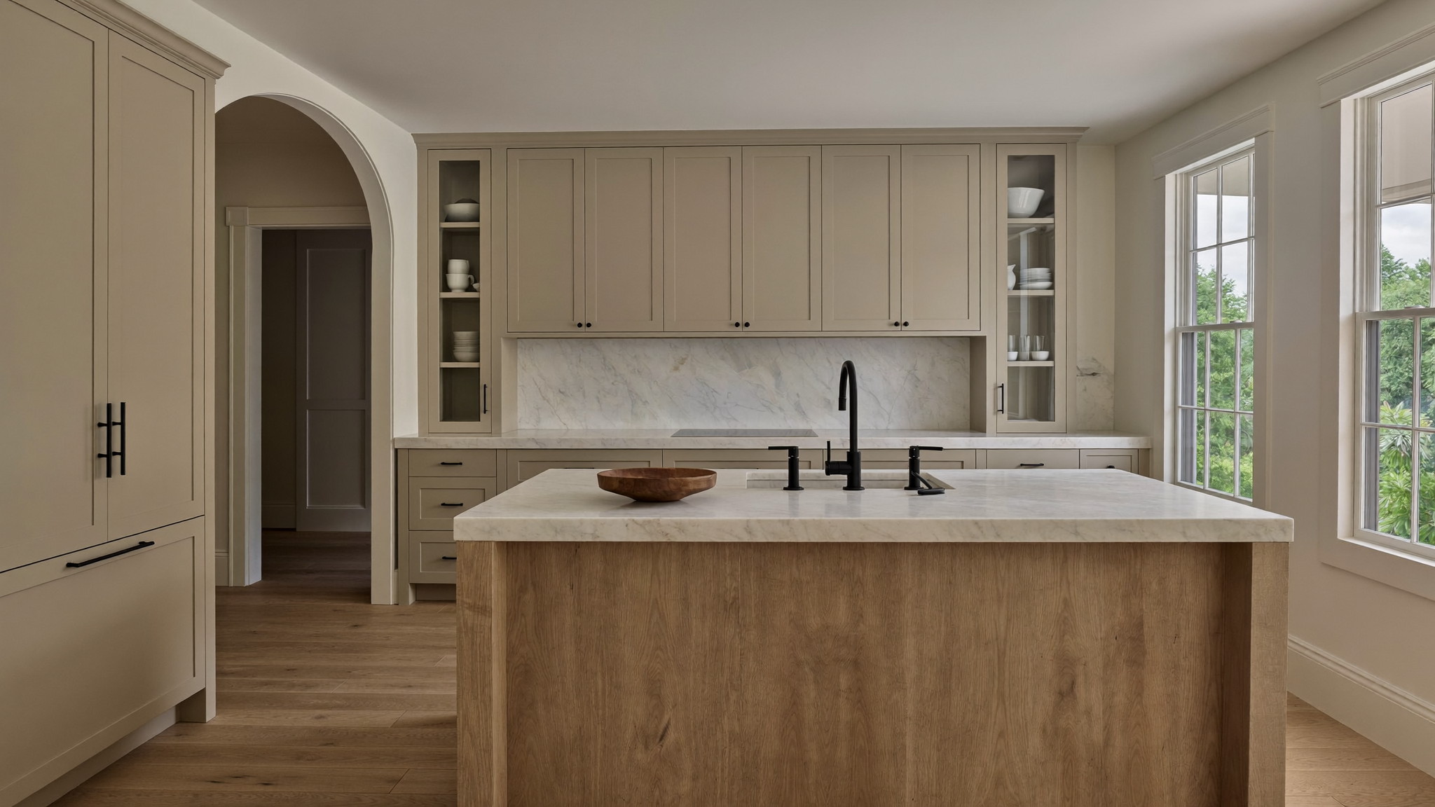Editorial photograph of a renovated family kitchen in an established Needham Massachusetts colonial: warm greige inset cabinetry, honed white stone
