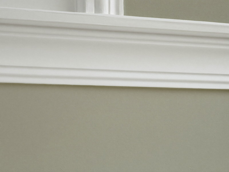 A razor-sharp masked paint line where a soft greige wall meets bright white crown molding, the edge perfectly straight and clean, smooth fresh paint on