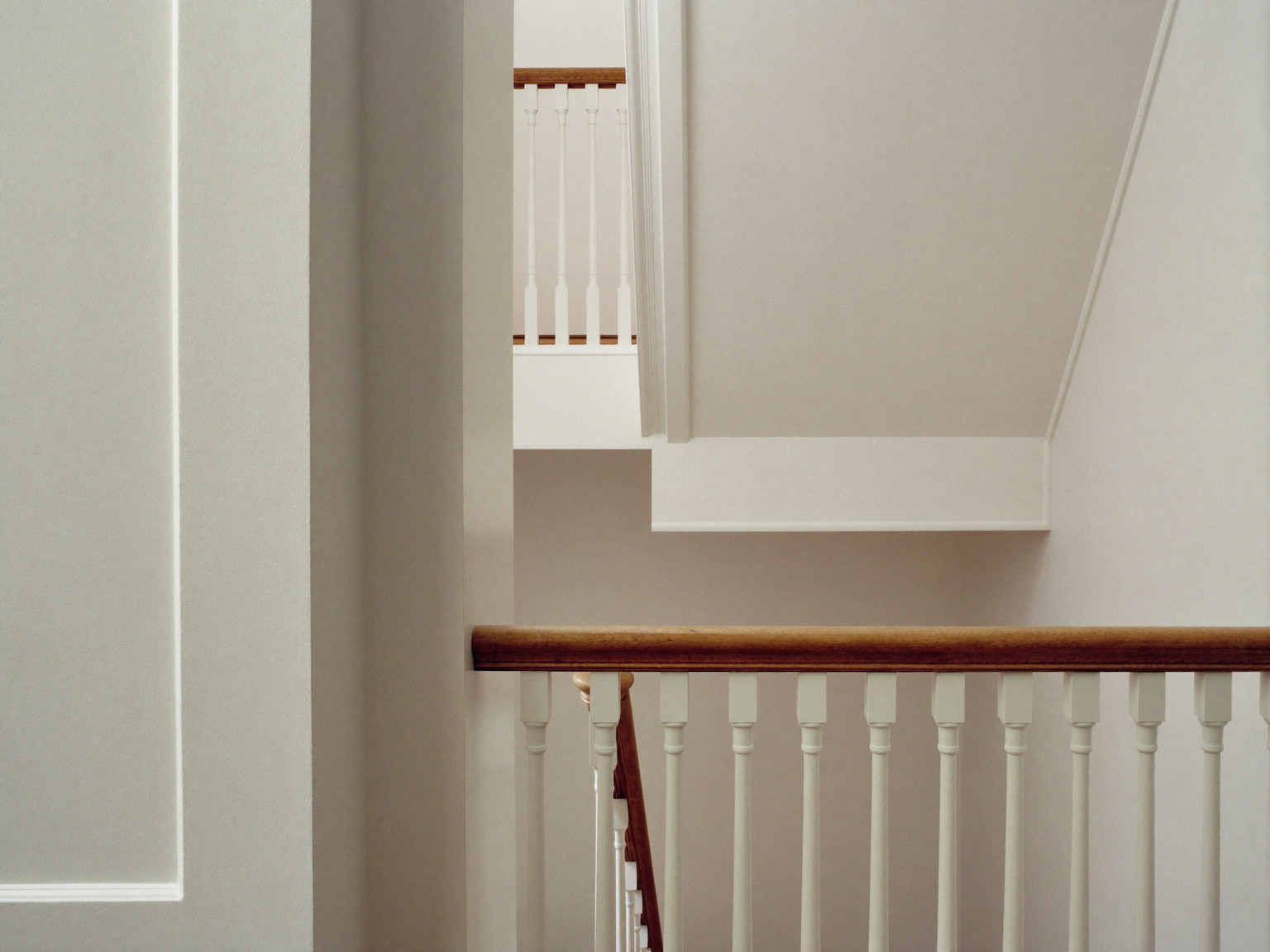 A finished repainted stair hall in an established Needham colonial: soft warm white walls over smooth restored plaster, bright white balusters with a
