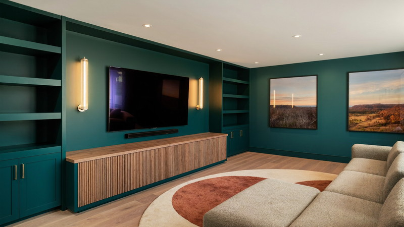 Finished Newton lower level with a deep teal built-in media wall, warm wood console, and comfortable sectional