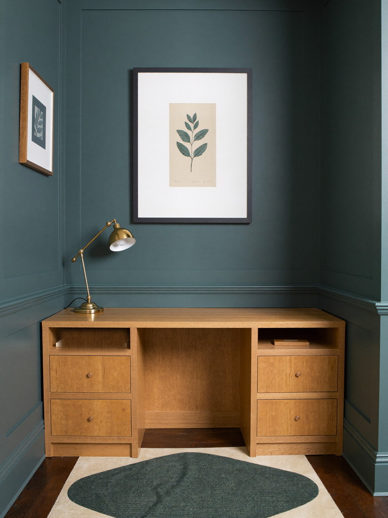 Quiet lower-level office nook with sage paneling, a walnut floating desk, and warm task lighting