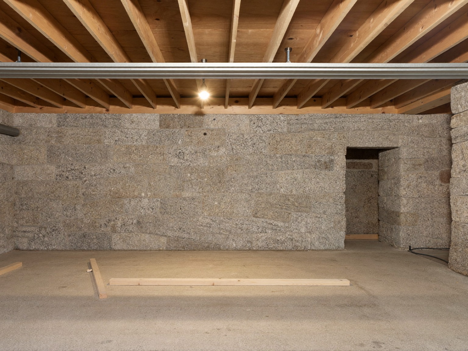Unfinished basement before build-out: fieldstone foundation wall, exposed joists, and bare concrete floor