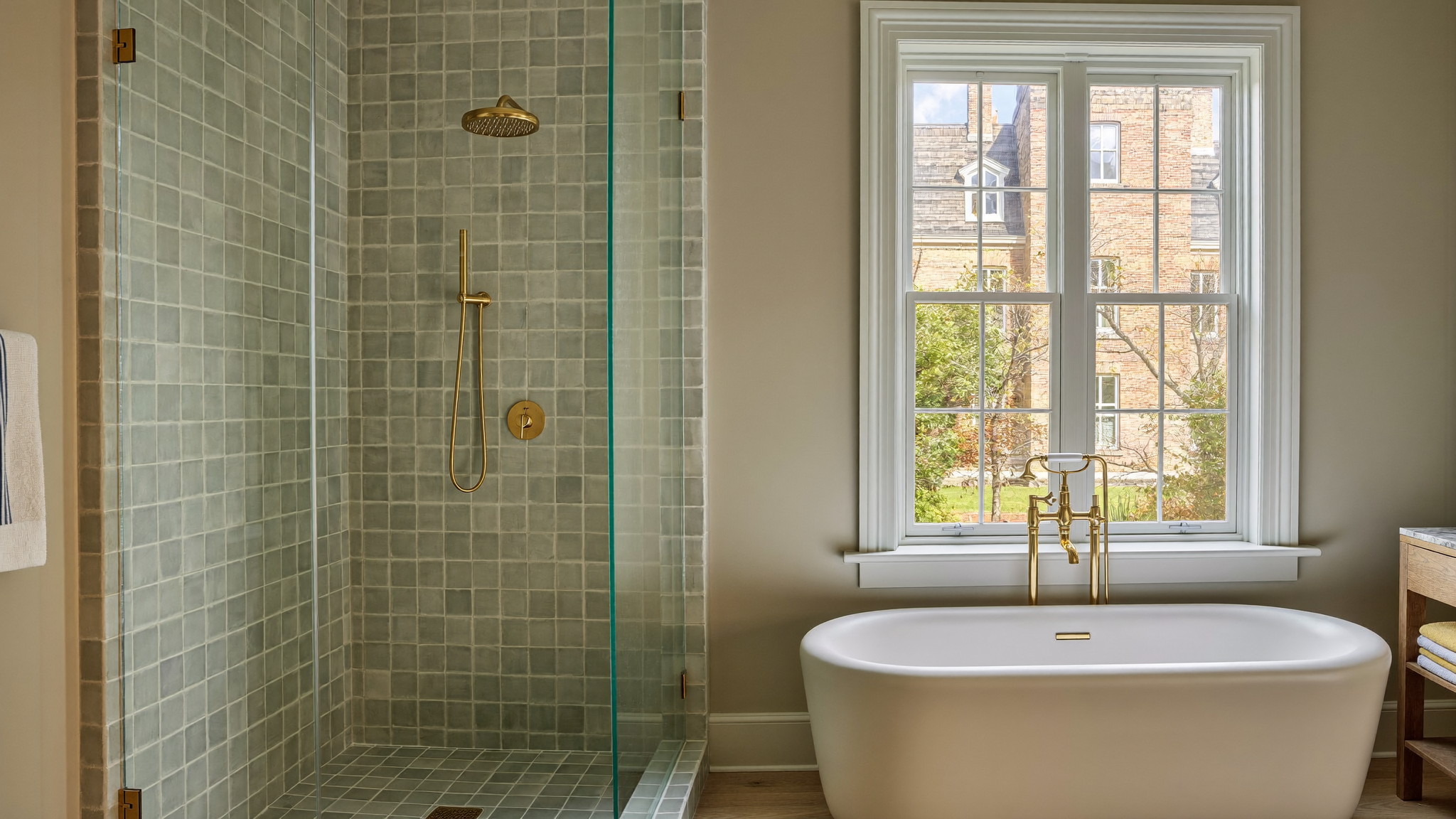 Curbless glass shower with soft sage tile and a freestanding oval tub beneath a tall window in a renovated Newton bathroom