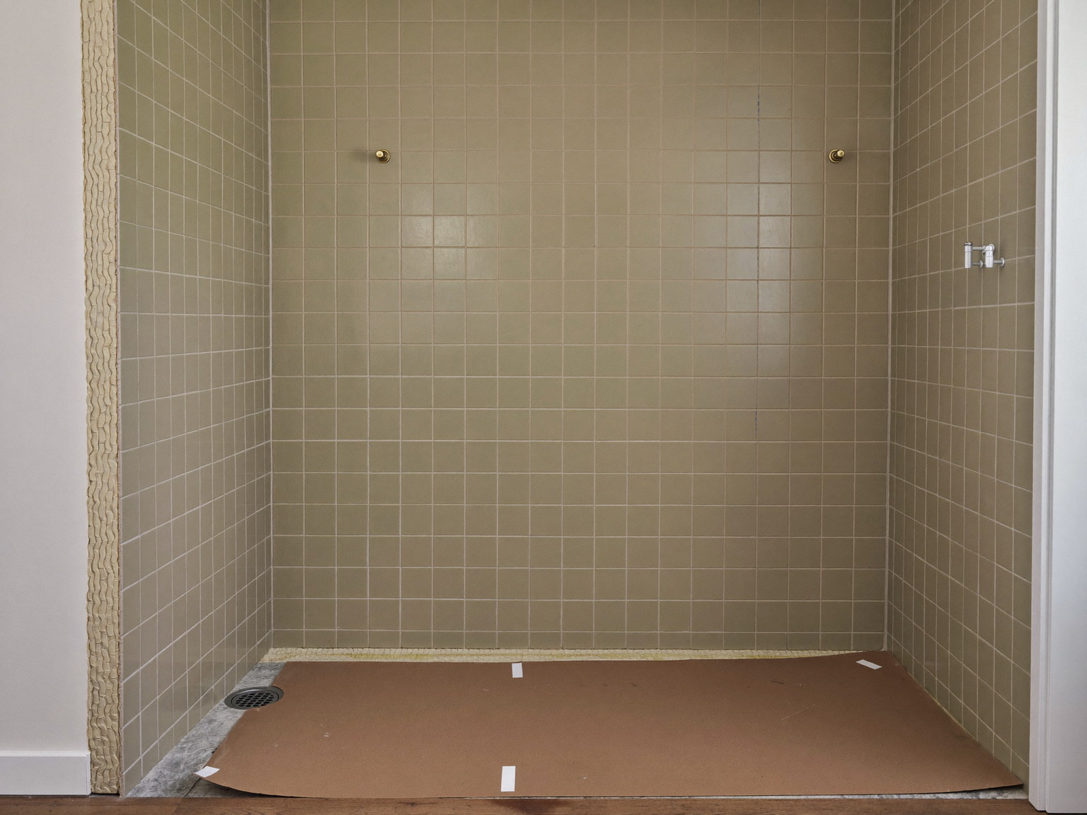 Shower walls newly tiled in sage with spacers set and waterproofing membrane visible at the edges