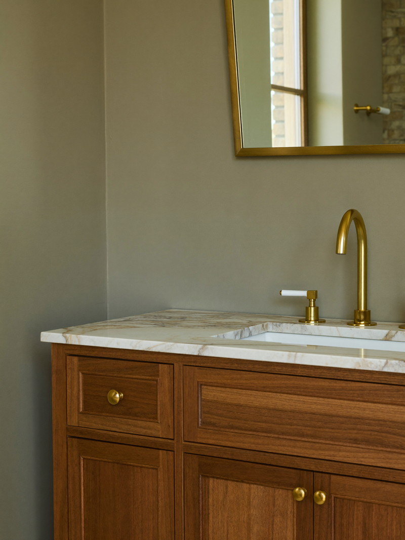 Furniture-style walnut vanity with honed carrara top, brass cross-handle faucet, and arched brass mirror