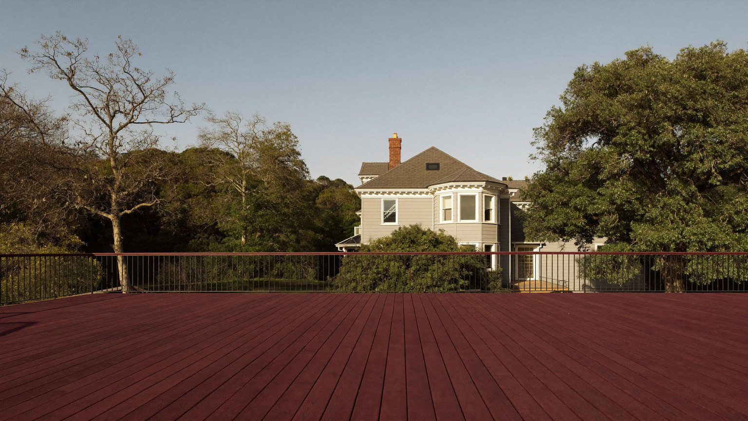 Freshly restained mahogany deck with slim black metal railings and an open view to a grey Victorian home