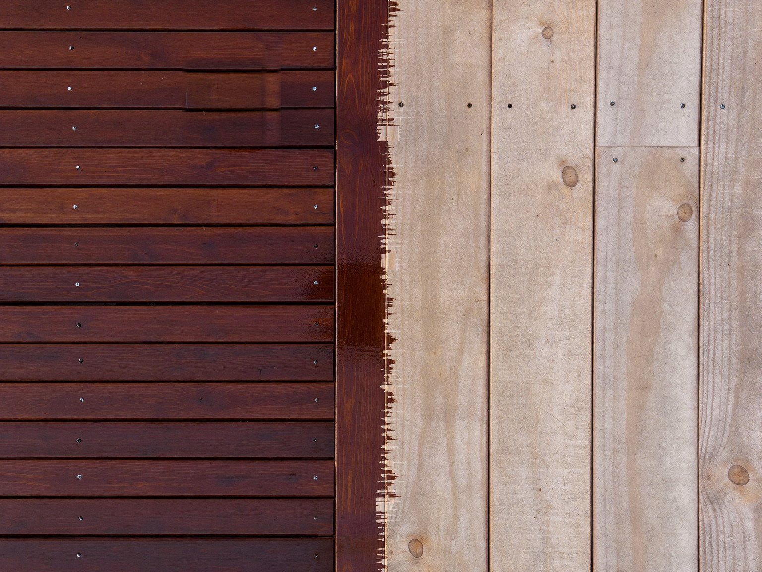 Deck restaining in progress: rich mahogany stain meeting bare sanded cedar at a crisp brushed line
