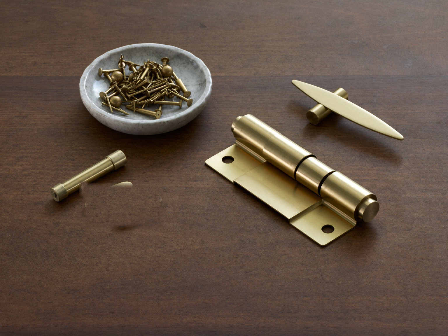 Brass hinges and quality door hardware laid out on dark stained wood