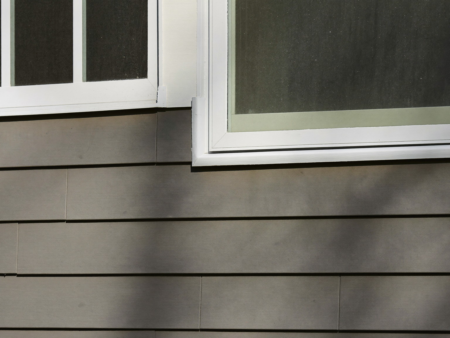 Fresh white caulk sealing the joint between grey clapboard siding and window trim after weatherproofing