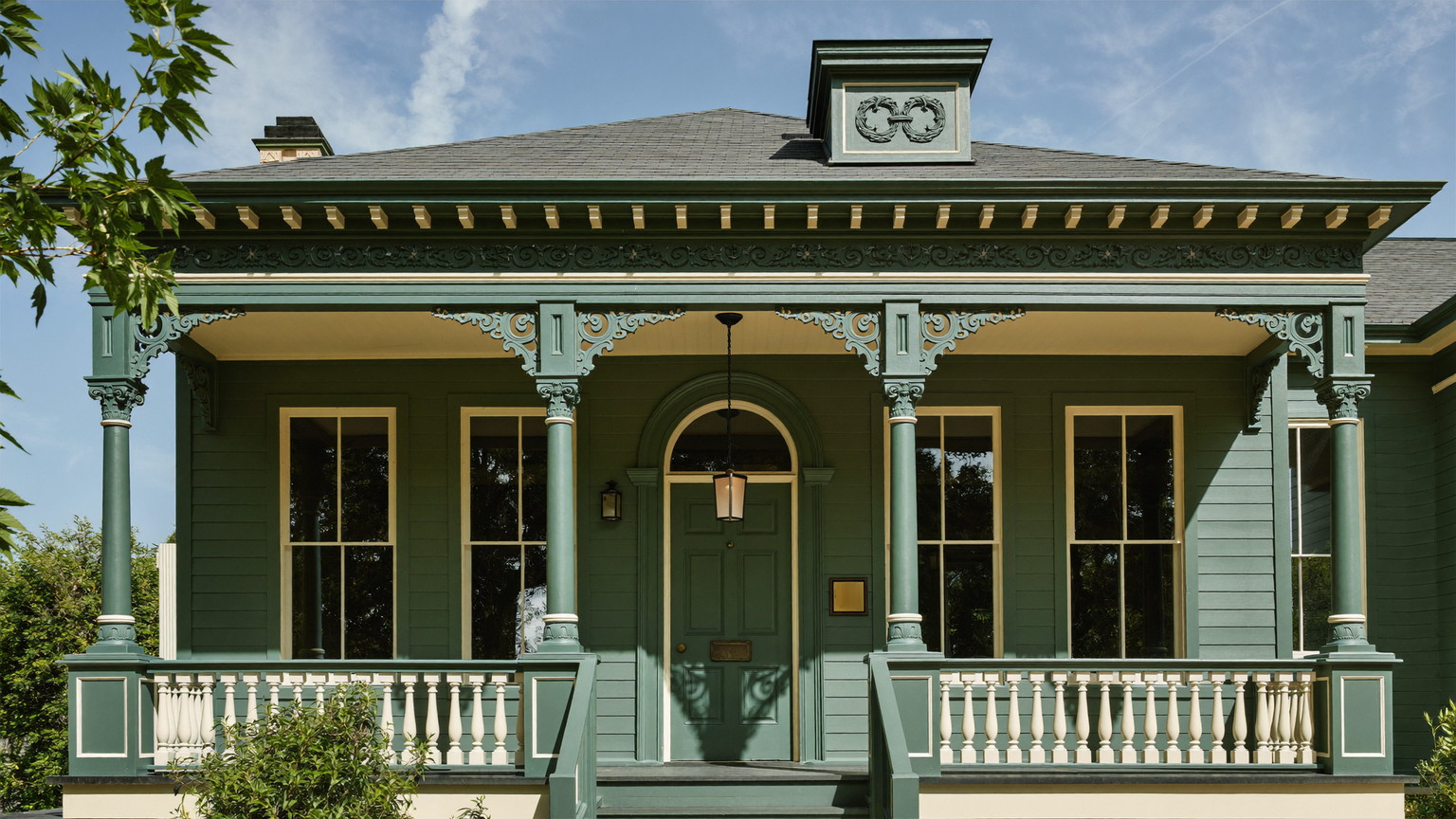 Freshly repainted sage-green Victorian entry with crisp white trim, columns, and porch detail