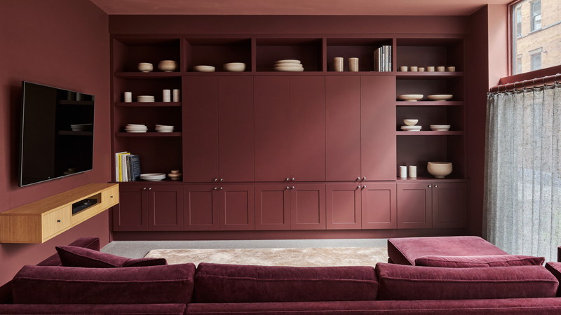 Finished brownstone garden-level lounge with a deep burgundy media wall and warm wood console