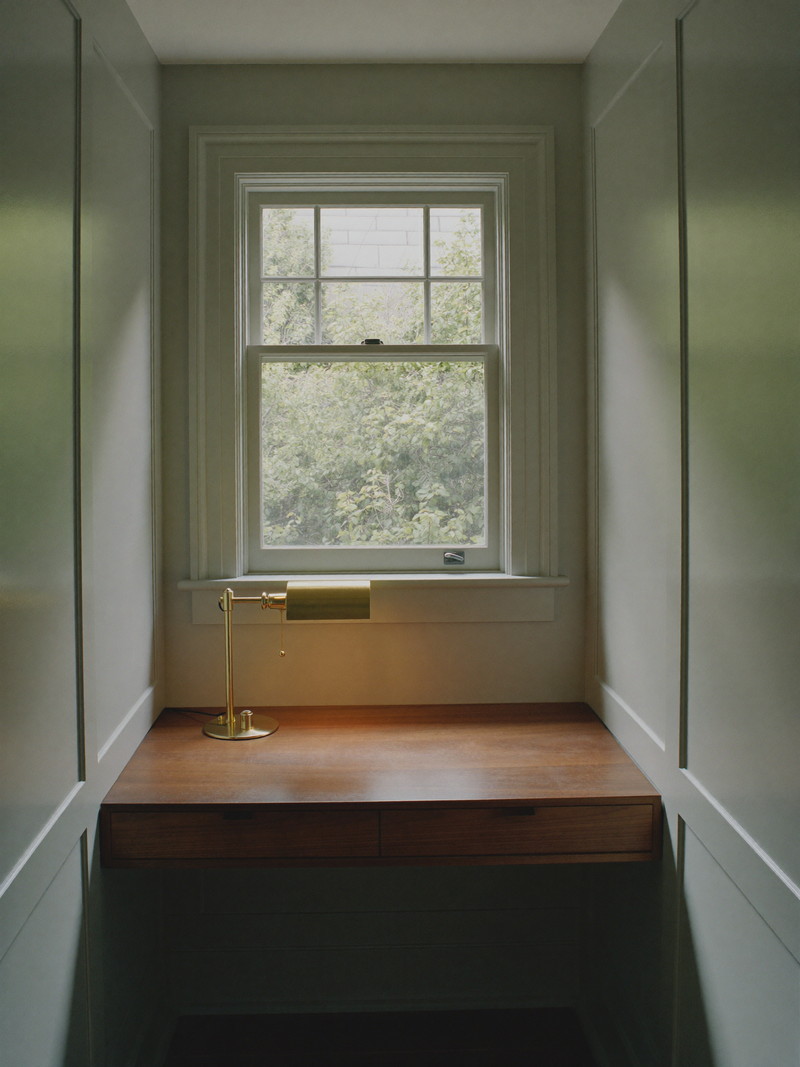 Quiet lower-level office nook with sage paneling, a walnut floating desk, and warm task lighting