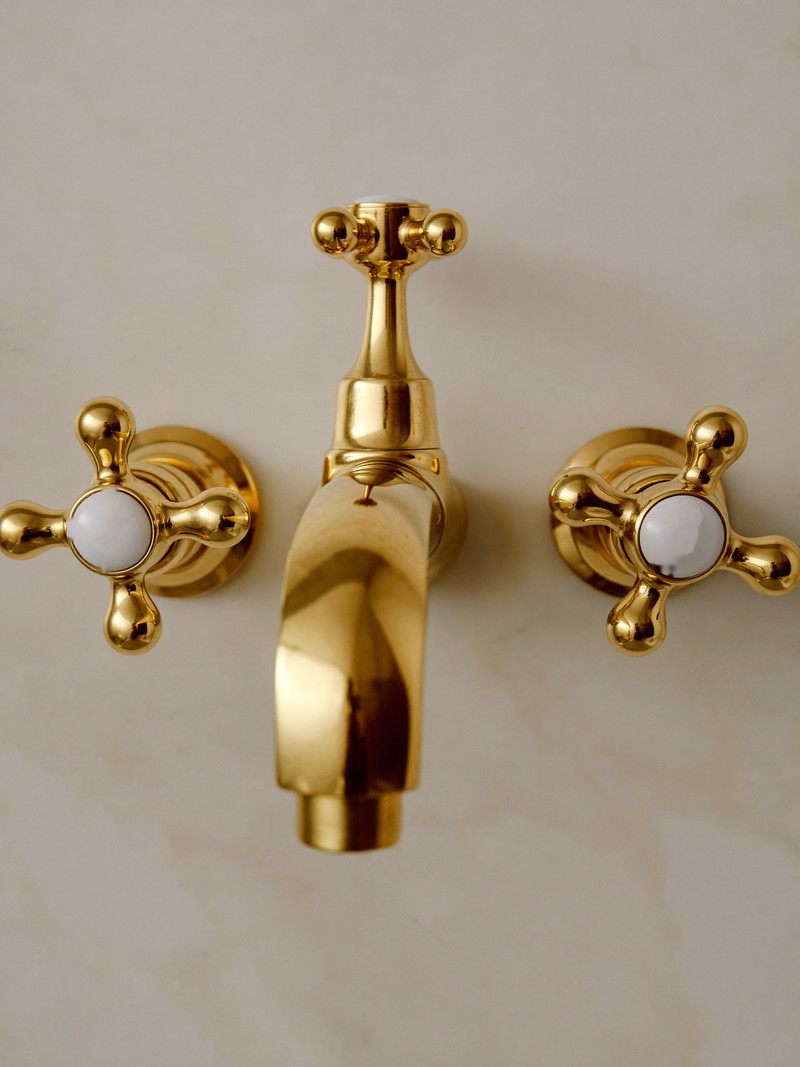 Polished brass bath spout and cross handles mounted on carrara marble