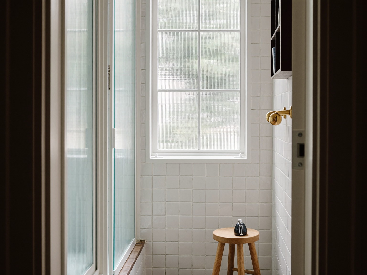 Calm plaster-white bathroom with a sage-tiled wet room behind fluted glass and a warm oak bench