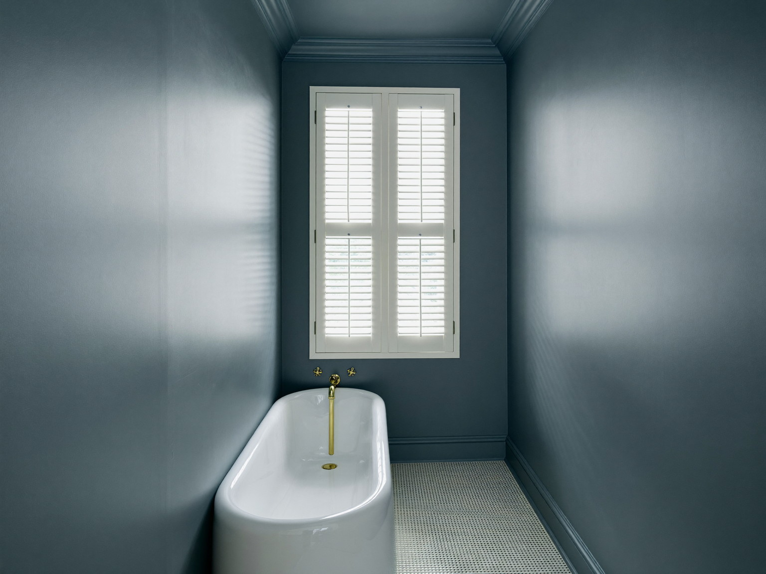 White freestanding tub under a bay of tall windows with sage wainscoting and a herringbone marble floor