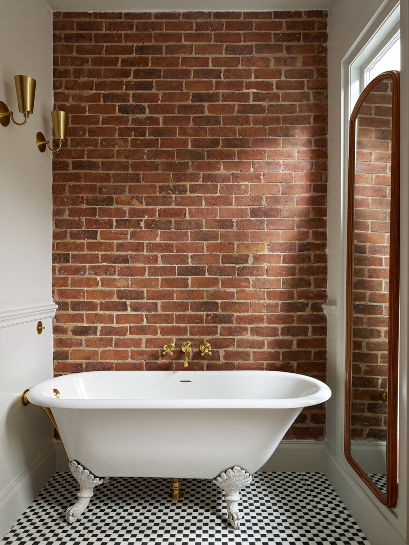 Deep olive-green bathroom with beadboard paneling, white hexagon mosaic floor, and brass sconces
