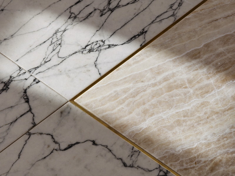 Honed carrara marble meeting sage ceramic tile with a crisp caulk line and brass trim strip