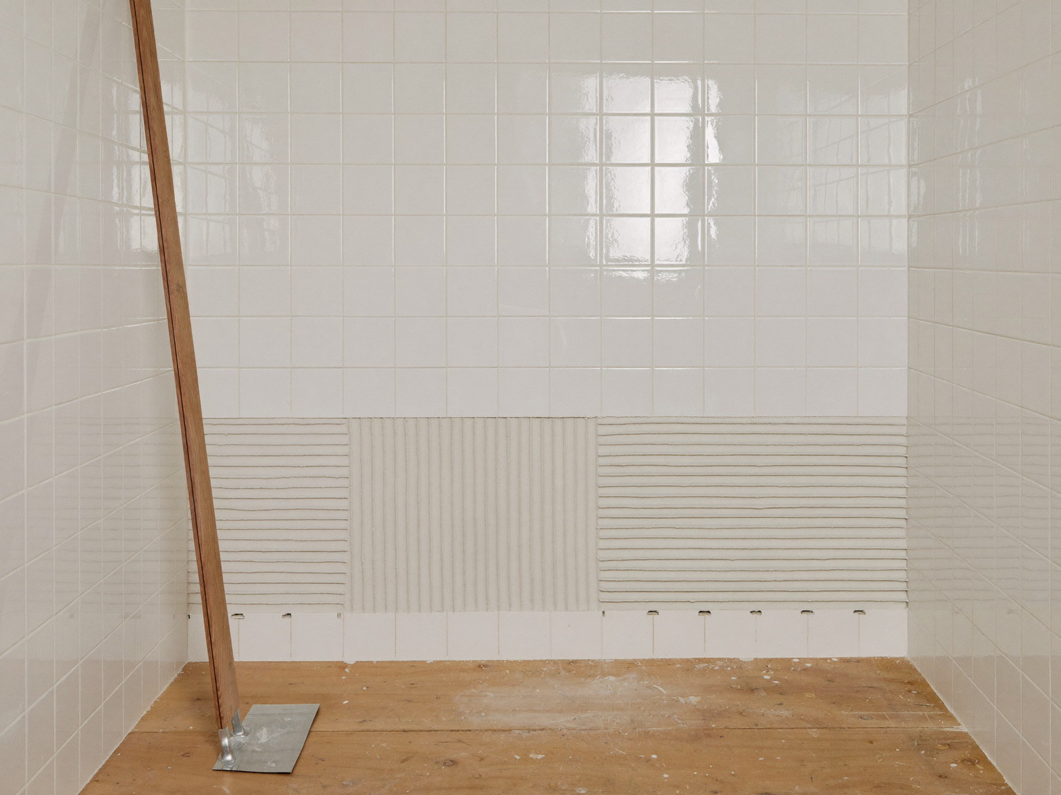 Shower walls newly tiled in sage with spacers set and waterproofing membrane visible at the edges