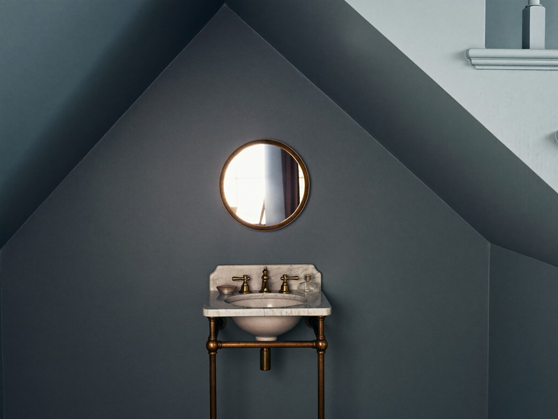 Powder room corner with a marble-topped brass washstand, round mirror, and deep sage paneled walls