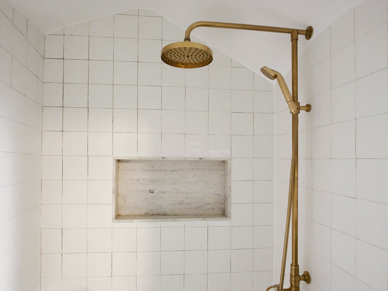 Walk-in shower with sage zellige-look tile, recessed marble niche, and brass rain head on a slide bar