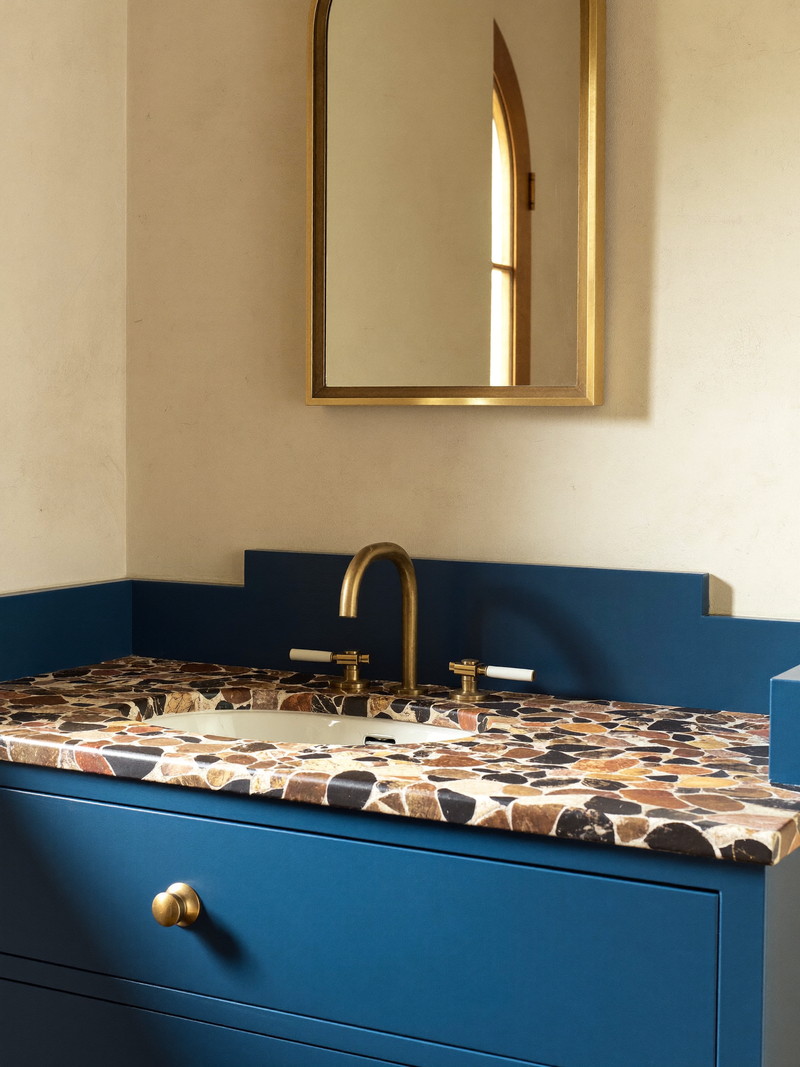 Furniture-style walnut vanity with honed carrara top, brass cross-handle faucet, and arched brass mirror