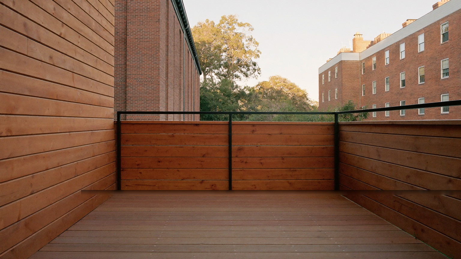 Freshly restained mahogany deck with slim black metal railings and an open view to a grey Victorian home