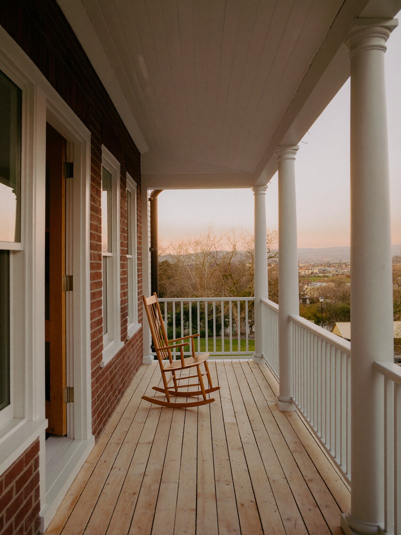 White farmer&rsquo;s porch with round columns, sky-blue beadboard ceiling, rocking chairs, and a stained wood floor