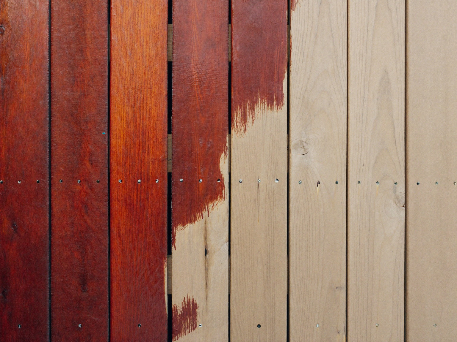 Deck restaining in progress: rich mahogany stain meeting bare sanded cedar at a crisp brushed line