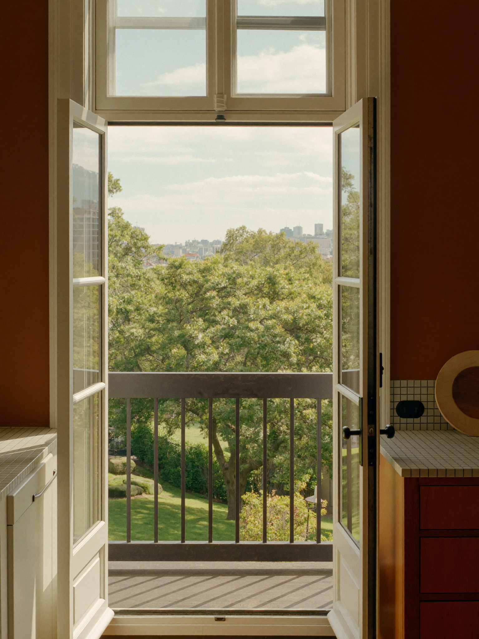 View through an open glass kitchen door onto a composite deck with black railings and green trees beyond