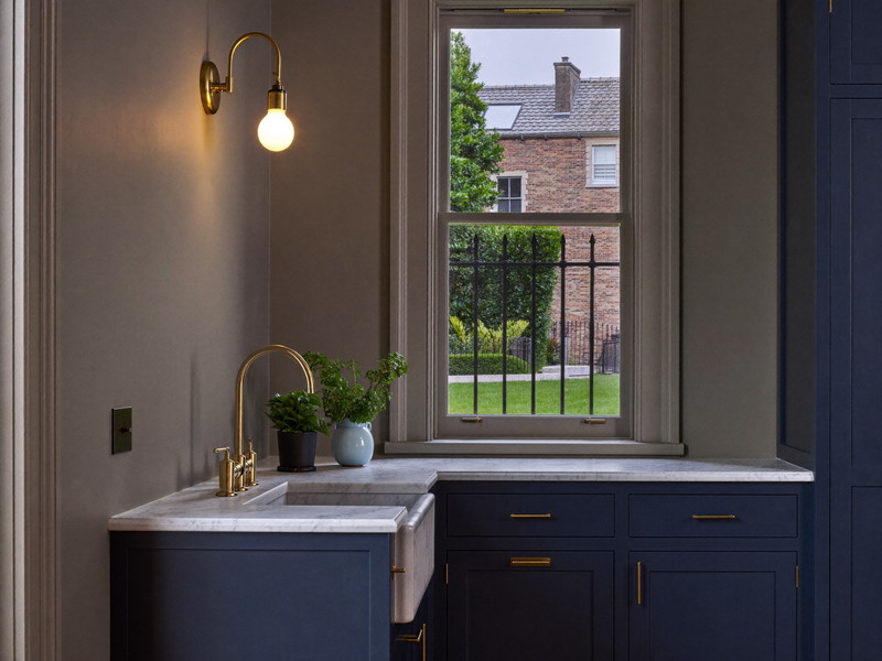 Corner of a finished colonial kitchen with cream cabinetry, butcher-block counter, and summer light outside