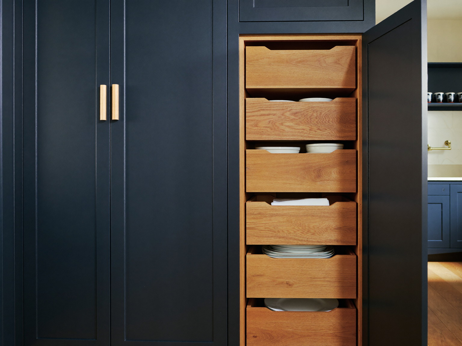 Custom pantry storage with oak-faced drawers and open shelves holding plain white ironstone dishes