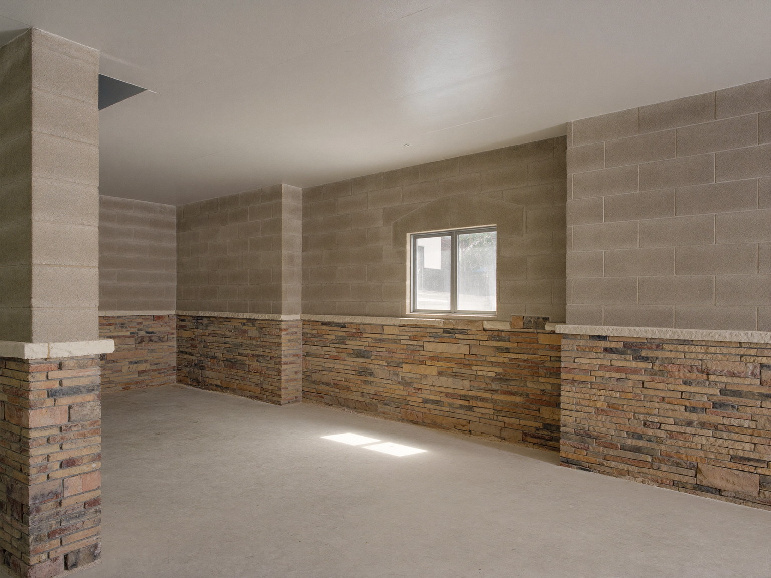 A clean unfinished basement in an older suburban home before renovation: stone and block foundation walls, smooth broom-swept concrete floor, a single small