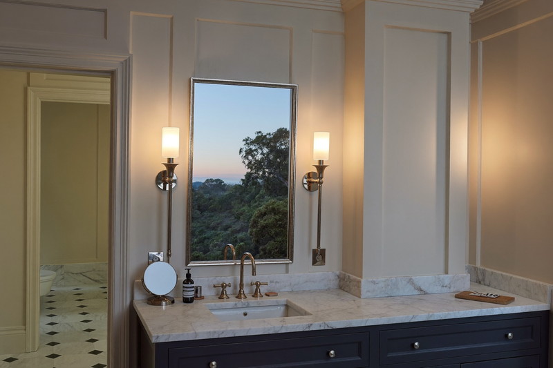 A calm finished colonial bathroom at dusk: polished nickel sconces lit beside a rectangular mirror, navy vanity, honed white marble top, marble subway tile