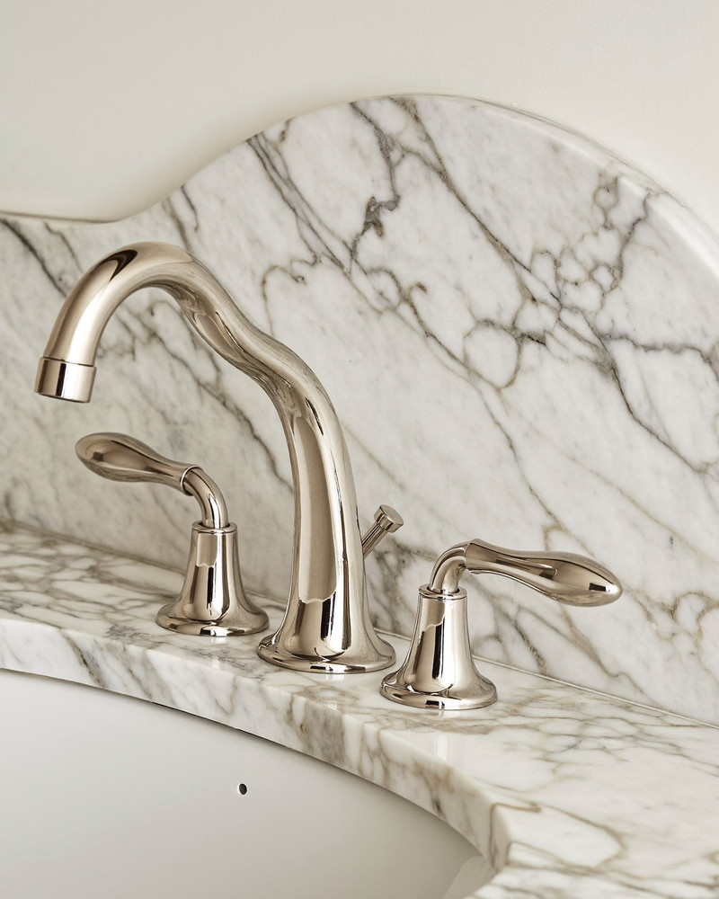 A polished nickel widespread bathroom faucet with a graceful curved spout and two classic handles on a honed white marble vanity top, macro view, soft window light