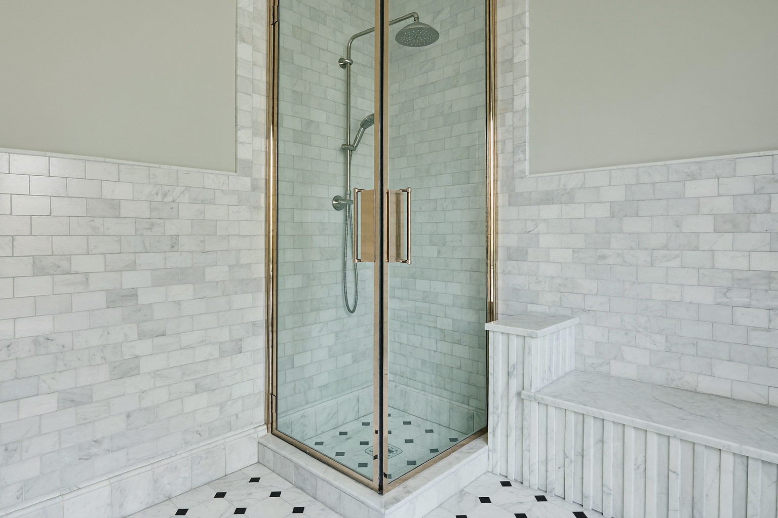 Wide photograph of a walk-in shower behind a polished nickel framed glass door in a renovated colonial bathroom: honed white marble subway tile walls, rain