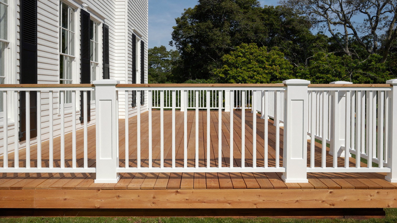 Editorial photograph of a rebuilt cedar-tone deck on the back of a classic Wellesley Massachusetts colonial: warm sealed cedar decking, crisp white square
