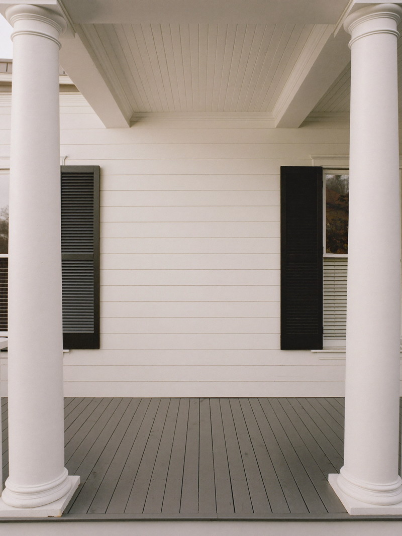 A restored front porch on a classic Wellesley colonial: round white columns, gray painted fir floor, white beadboard ceiling, white clapboard wall with