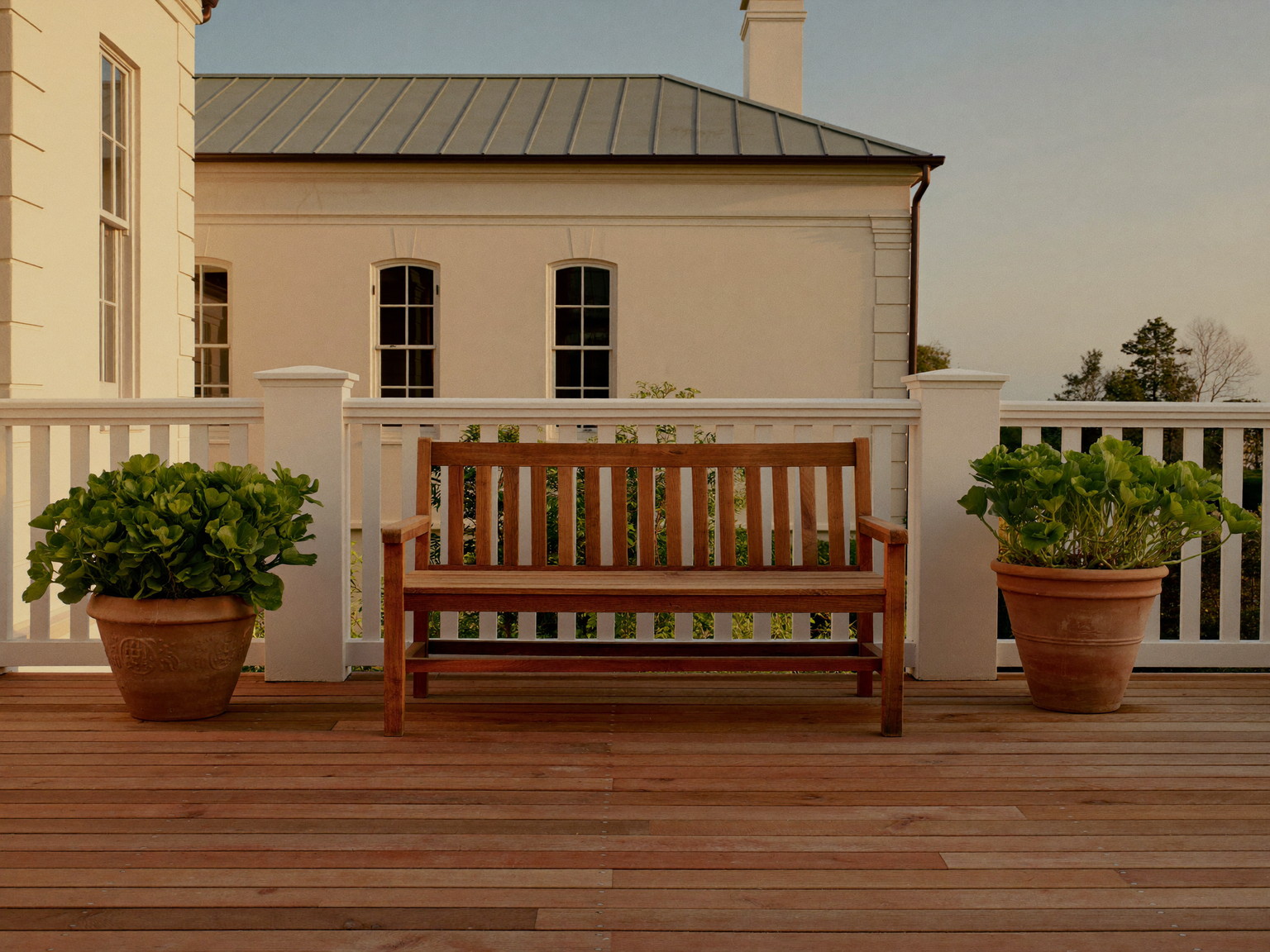 A finished cedar deck off the back of a classic Wellesley colonial at golden hour: warm sealed cedar decking, white rail with square balusters, a simple teak